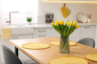 Photo of Spring interior. Bouquet of beautiful yellow tulips on wooden table in stylish kitchen, space for text