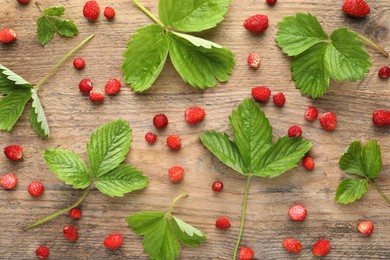 Many fresh wild strawberries and leaves on wooden table, flat lay