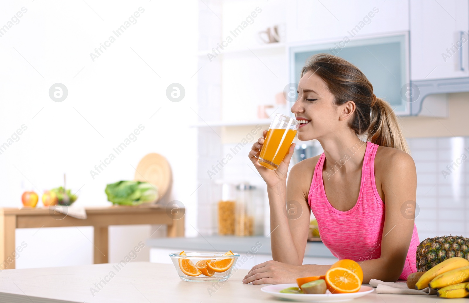 Photo of Woman with glass of orange juice at table in kitchen. Healthy diet