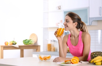 Woman with glass of orange juice at table in kitchen. Healthy diet