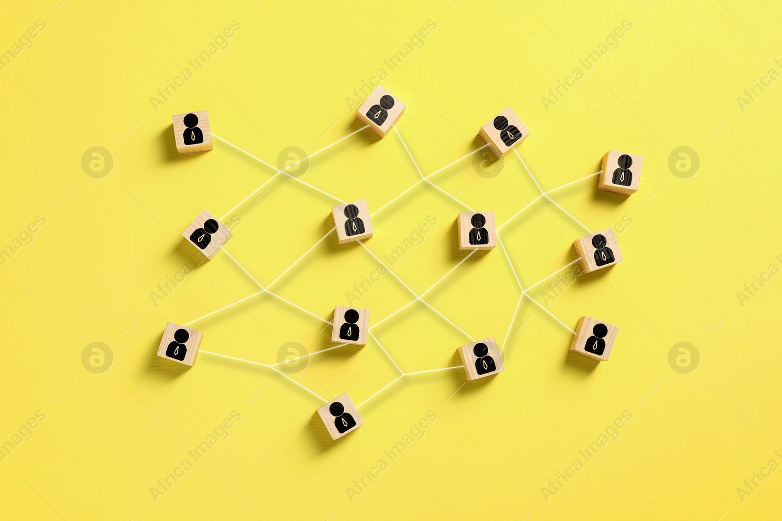 Image of Teamwork. Wooden cubes with human icons linked together symbolizing cooperation on yellow background, top view