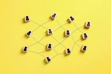 Teamwork. Wooden cubes with human icons linked together symbolizing cooperation on yellow background, top view