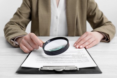 Woman looking at document through magnifier at wooden table, closeup. Searching concept