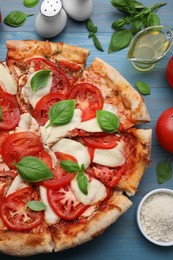 Photo of Delicious Caprese pizza and ingredients on blue wooden table, flat lay