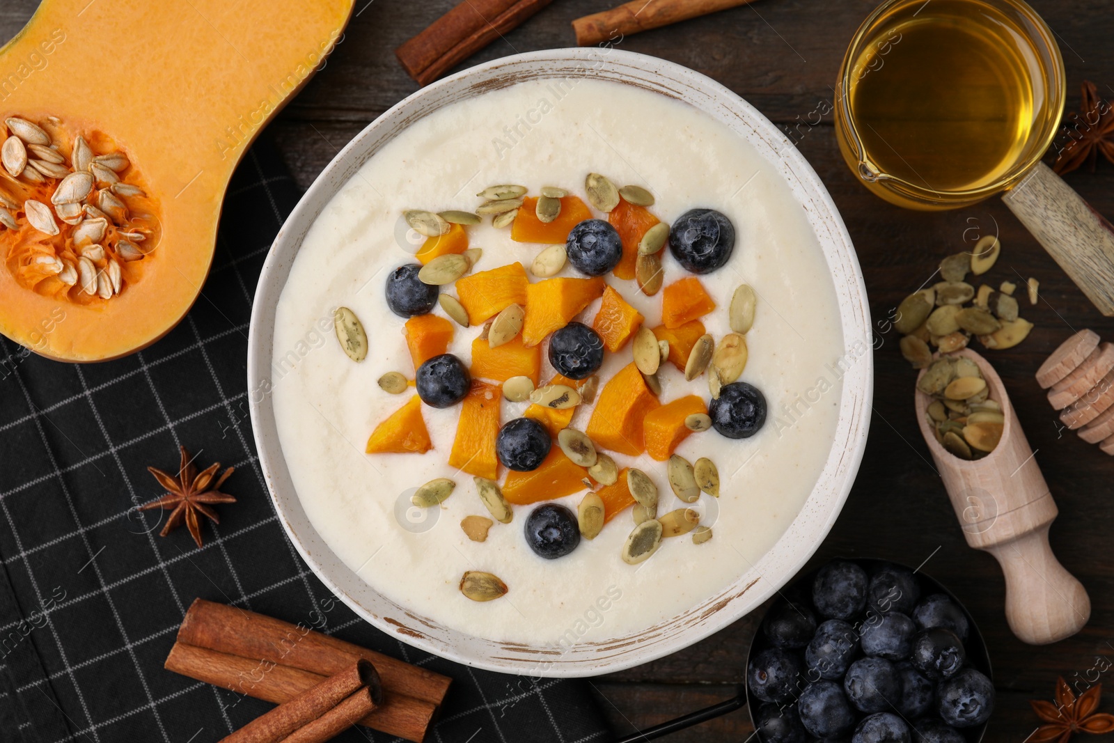 Photo of Bowl of delicious semolina pudding with blueberries, pumpkin and ingredients on table, flat lay