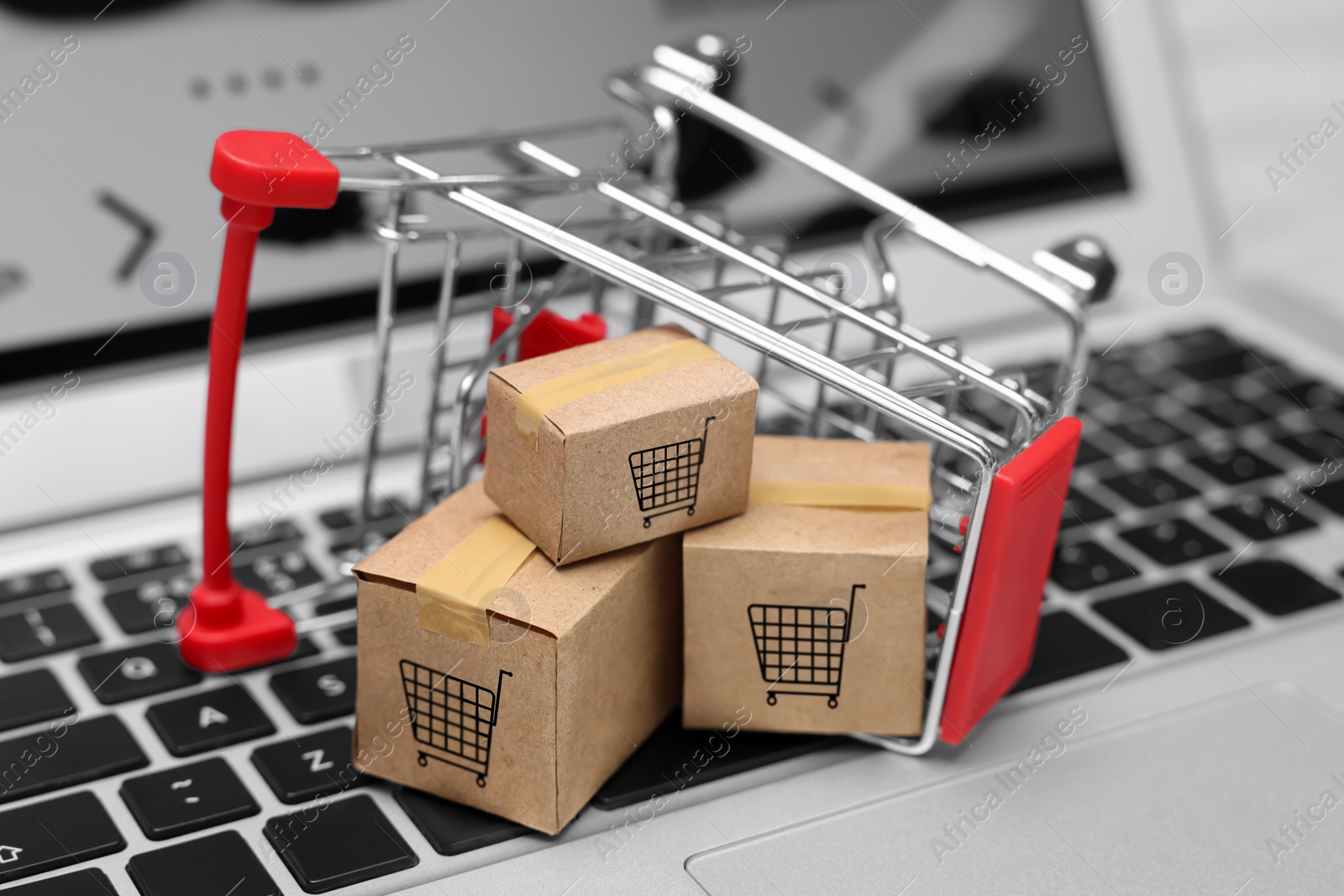 Image of Internet store. Small cardboard boxes and shopping cart on laptop, closeup