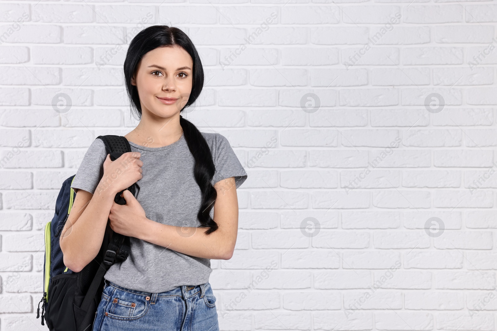 Photo of Student with backpack near white brick wall. Space for text