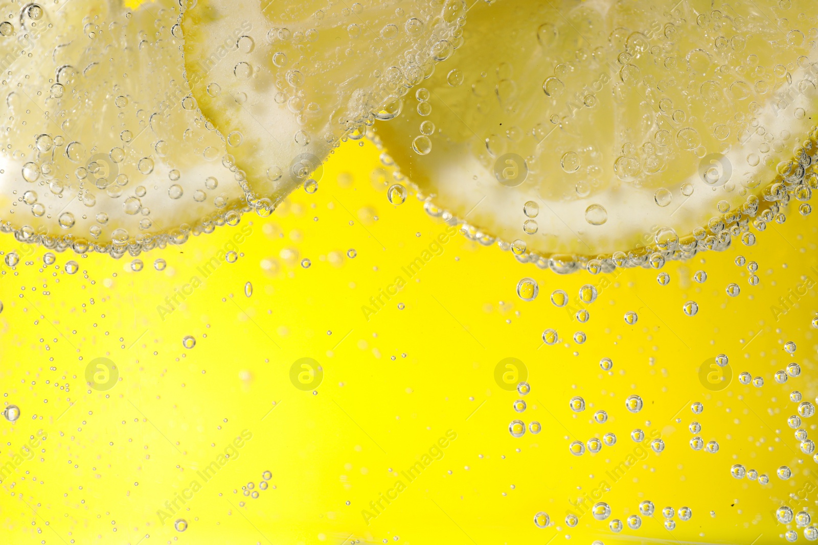 Photo of Juicy lemon slices in soda water against yellow background, closeup. Space for text