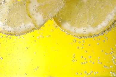 Photo of Juicy lemon slices in soda water against yellow background, closeup. Space for text
