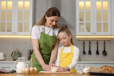 Photo of Making bread. Mother and her daughter kneading dough at wooden table in kitchen