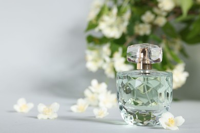 Photo of Aromatic perfume in bottle and beautiful jasmine flowers on grey background, closeup. Space for text