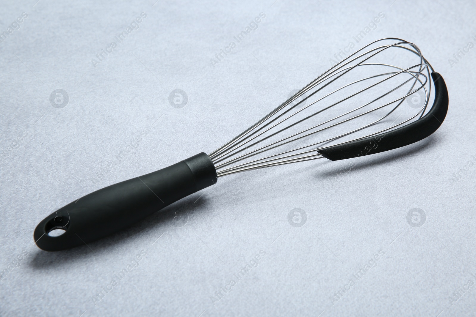 Photo of Metal whisk on gray table. Kitchen tool