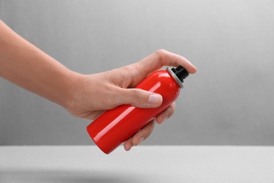 Woman with bottle of insect repellent spray on grey background, closeup