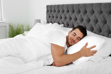 Young man sleeping in bed with soft pillows at home