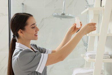 Photo of Chambermaid putting bottle of shampoo on shelf in hotel bathroom