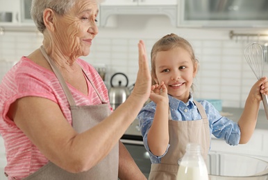 Photo of Cute girl and her grandmother cooking in kitchen