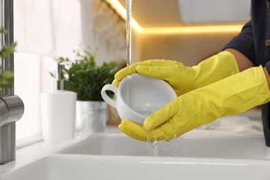 Woman washing cup at sink in kitchen, closeup