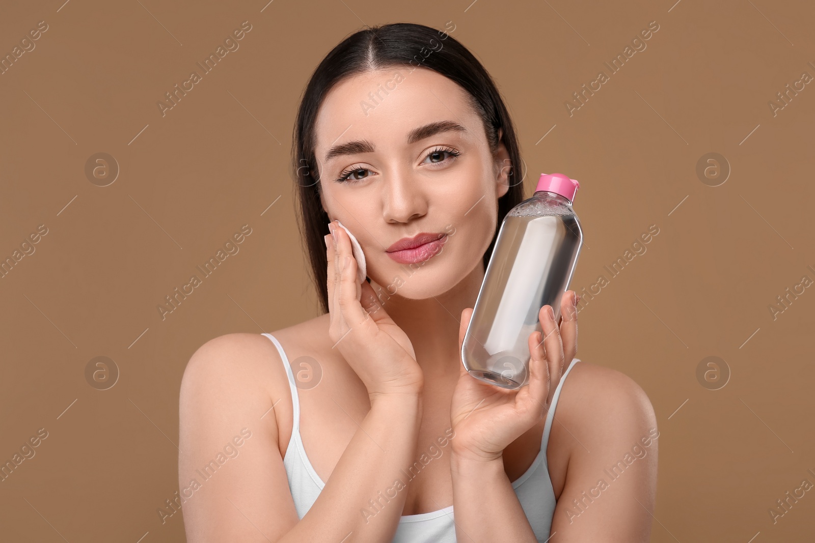 Photo of Beautiful woman removing makeup with cotton pad on beige background