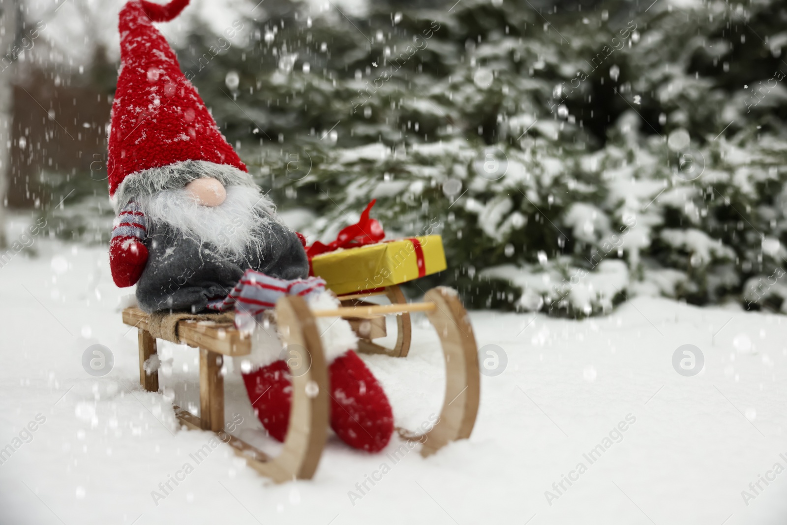 Photo of Wooden sleighs with Christmas gnome and gift box on snow outdoors. Space for text