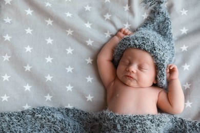 Cute newborn baby in warm hat sleeping on bed, top view. Space for text