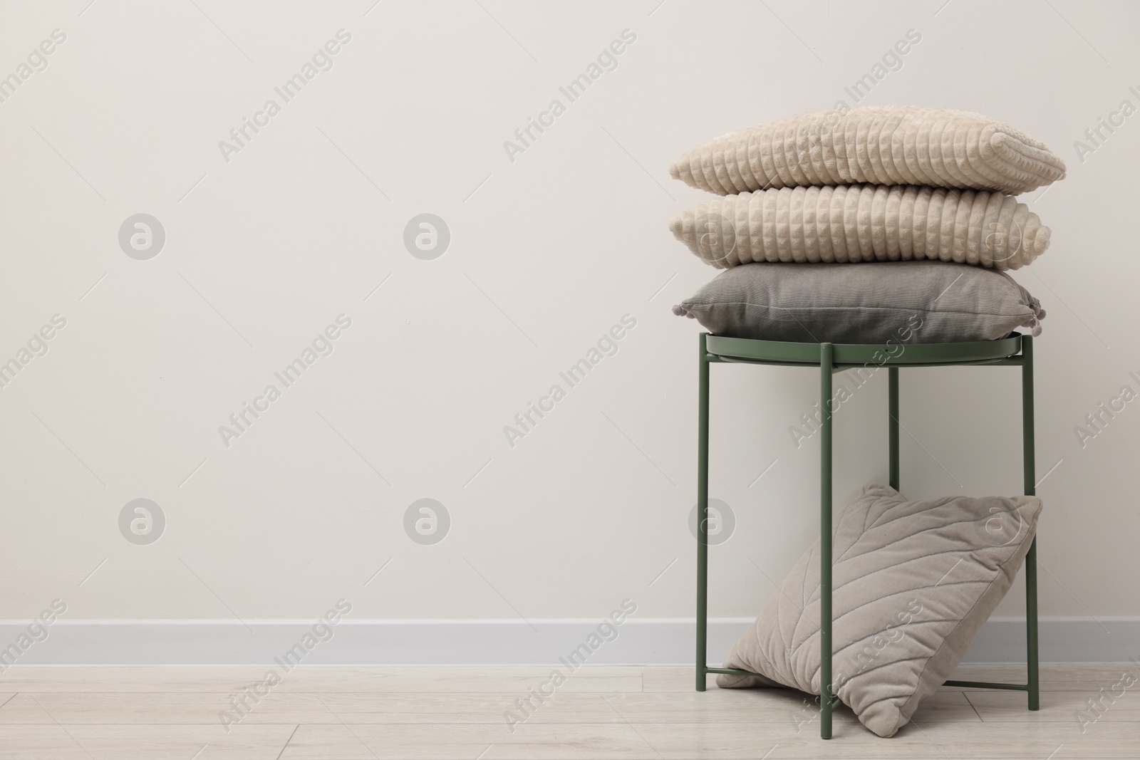 Photo of Soft pillows and side table near beige wall indoors, space for text
