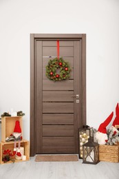 Photo of Christmas wreath hanging on wooden door and festive decoration indoors