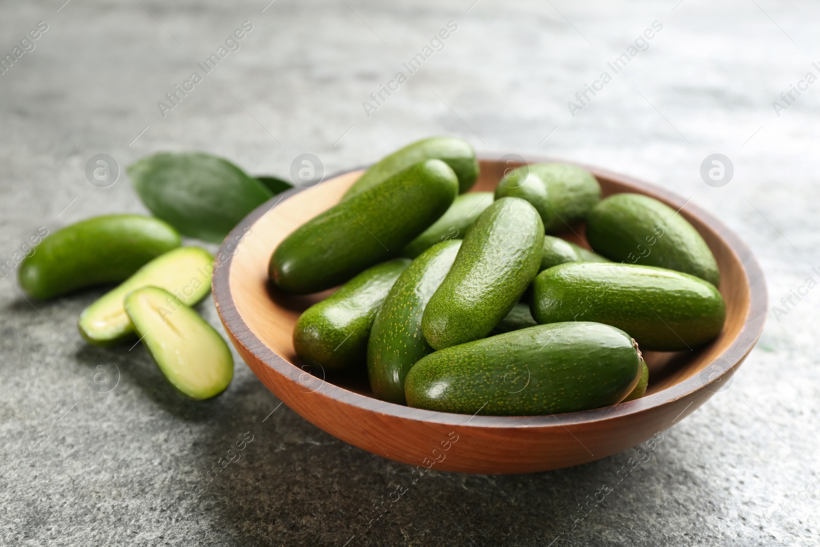 Photo of Fresh seedless avocados in wooden bowl on grey table, closeup