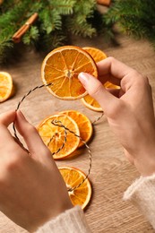 Woman making handmade garland from dry orange slices at wooden table, closeup