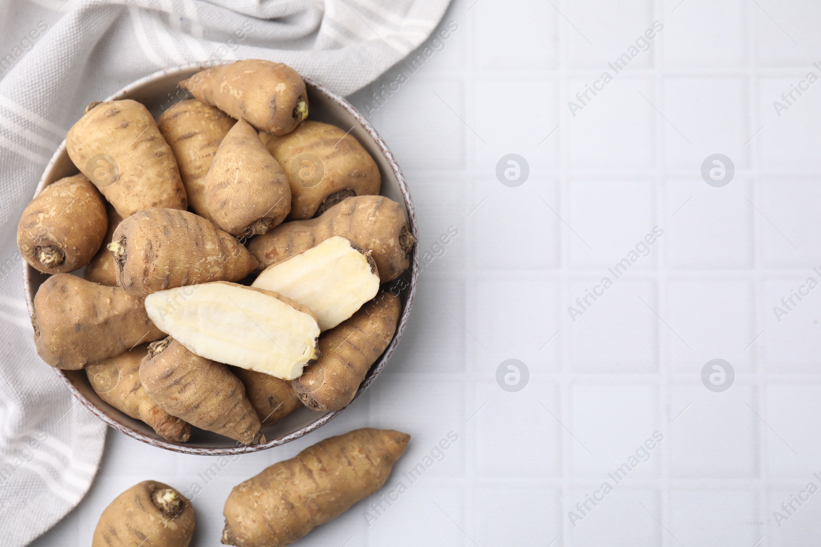 Photo of Whole and cut tubers of turnip rooted chervil in bowl on white tiled table, top view. Space for text