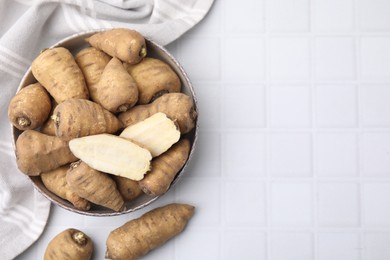 Whole and cut tubers of turnip rooted chervil in bowl on white tiled table, top view. Space for text