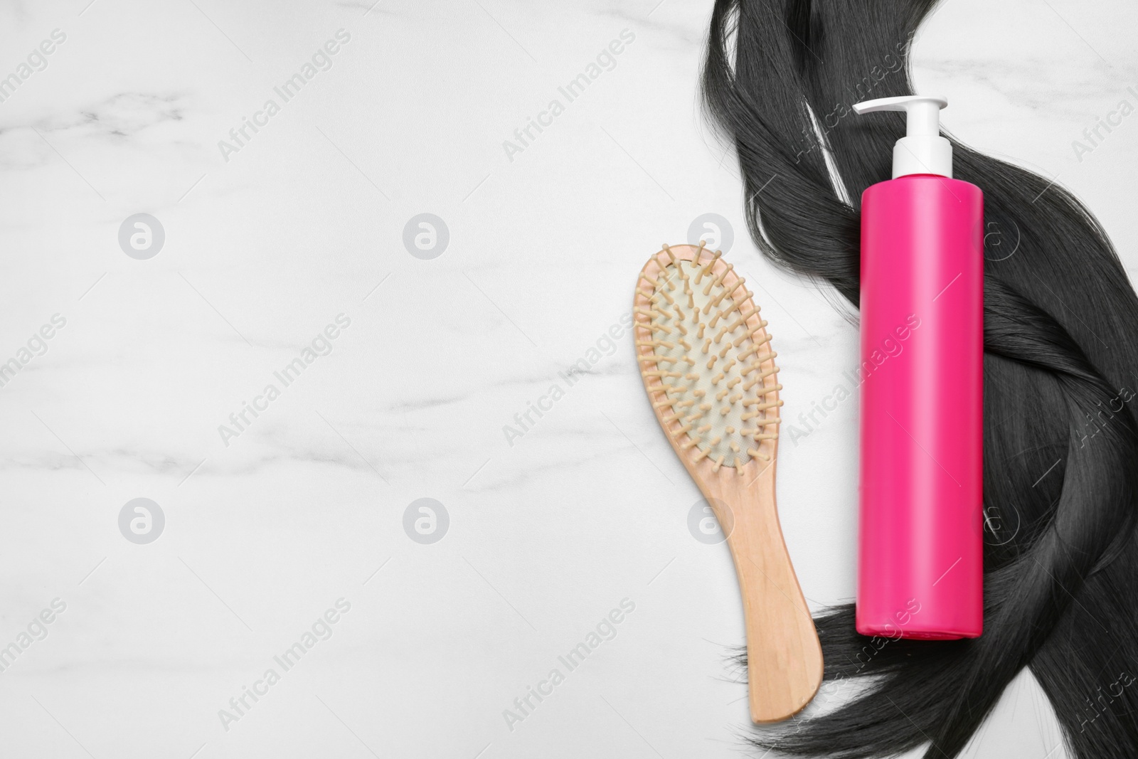 Photo of Spray bottle with thermal protection, lock of brunette hair and hairbrush on white marble table, flat lay. Space for text