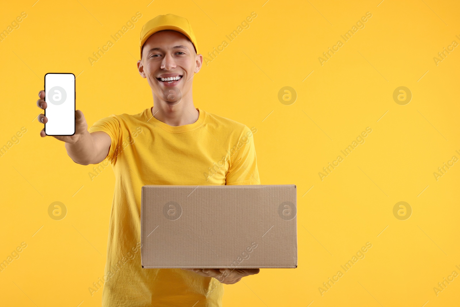 Photo of Happy courier with parcel and smartphone on orange background. Space for text