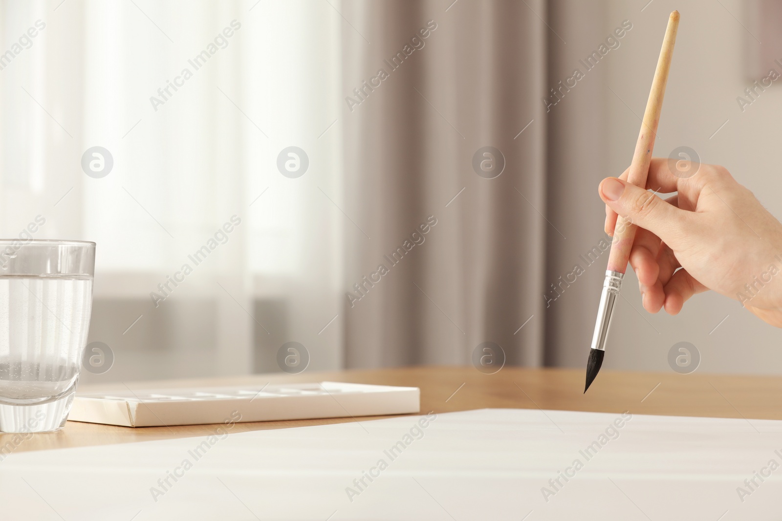 Photo of Woman with brush at wooden table indoors, closeup and space for text. Watercolor artwork