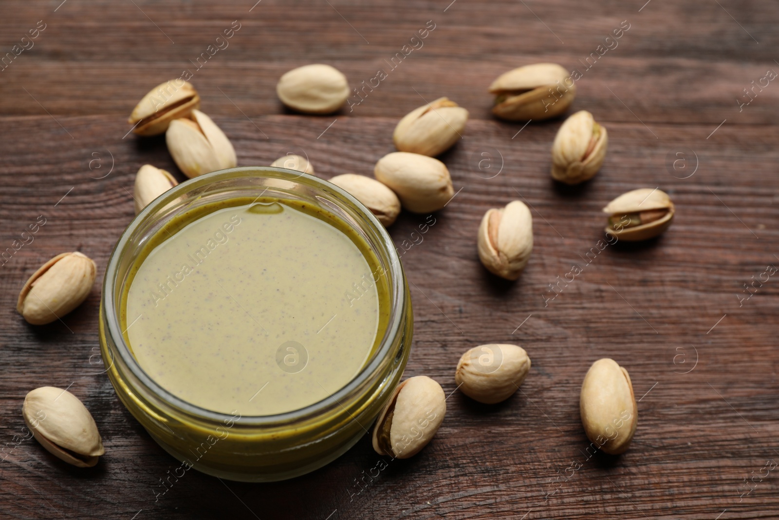 Photo of Delicious pistachio butter and ingredients on wooden table, closeup