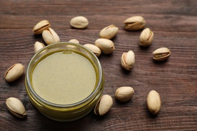 Photo of Delicious pistachio butter and ingredients on wooden table, closeup