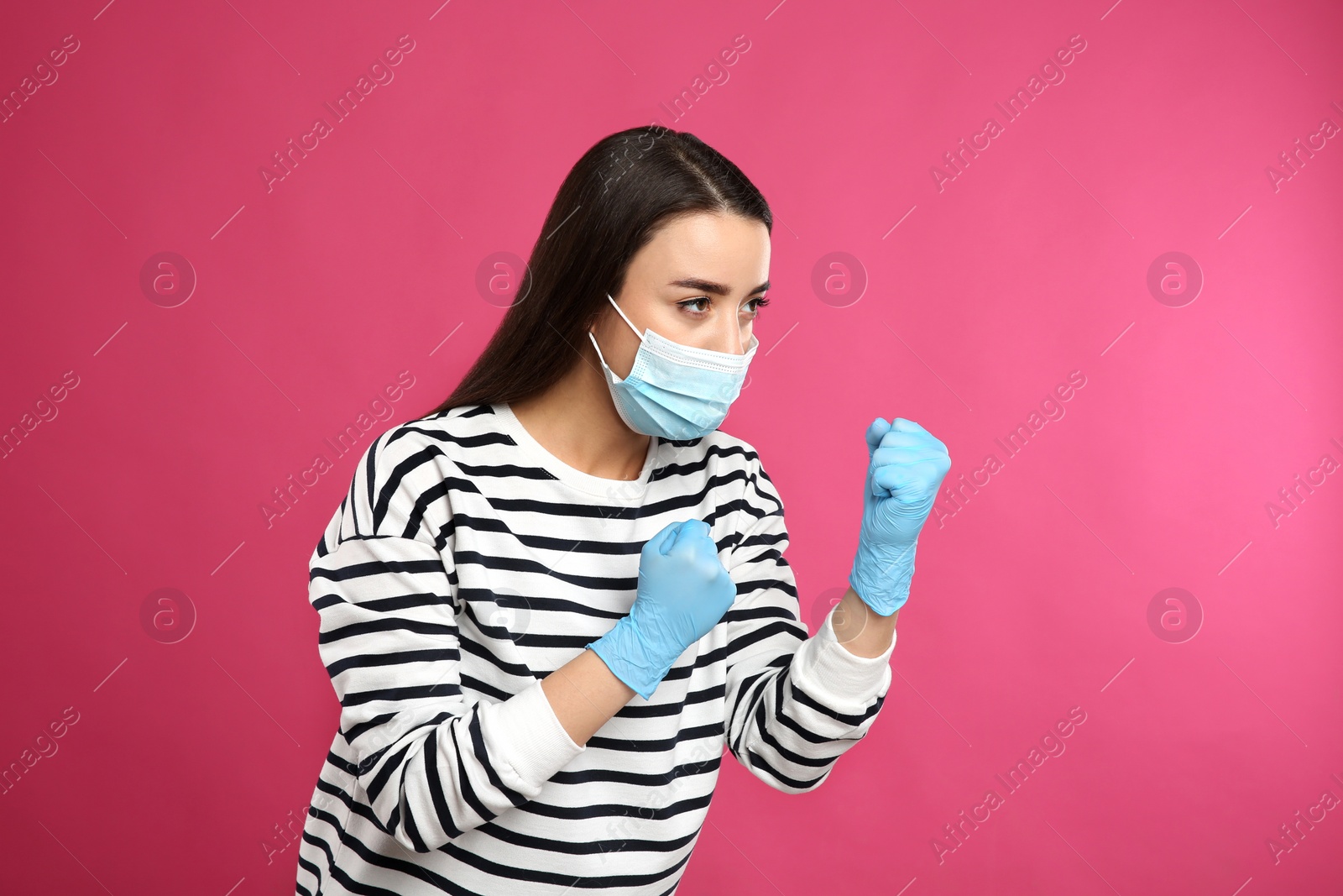 Photo of Woman with protective mask and gloves in fighting pose on pink background. Strong immunity concept