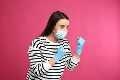 Photo of Woman with protective mask and gloves in fighting pose on pink background. Strong immunity concept