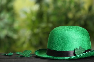 Leprechaun hat and clover leaves on wooden table against blurred background, space for text. St Patrick's Day celebration