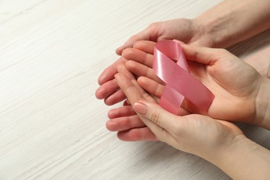 Photo of Breast cancer awareness. Women holding pink ribbon at white wooden table, closeup. Space for text