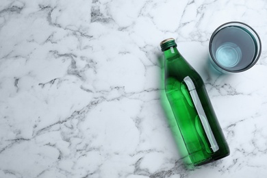 Photo of Glass and bottle with water on white marble background, flat lay. Space for text