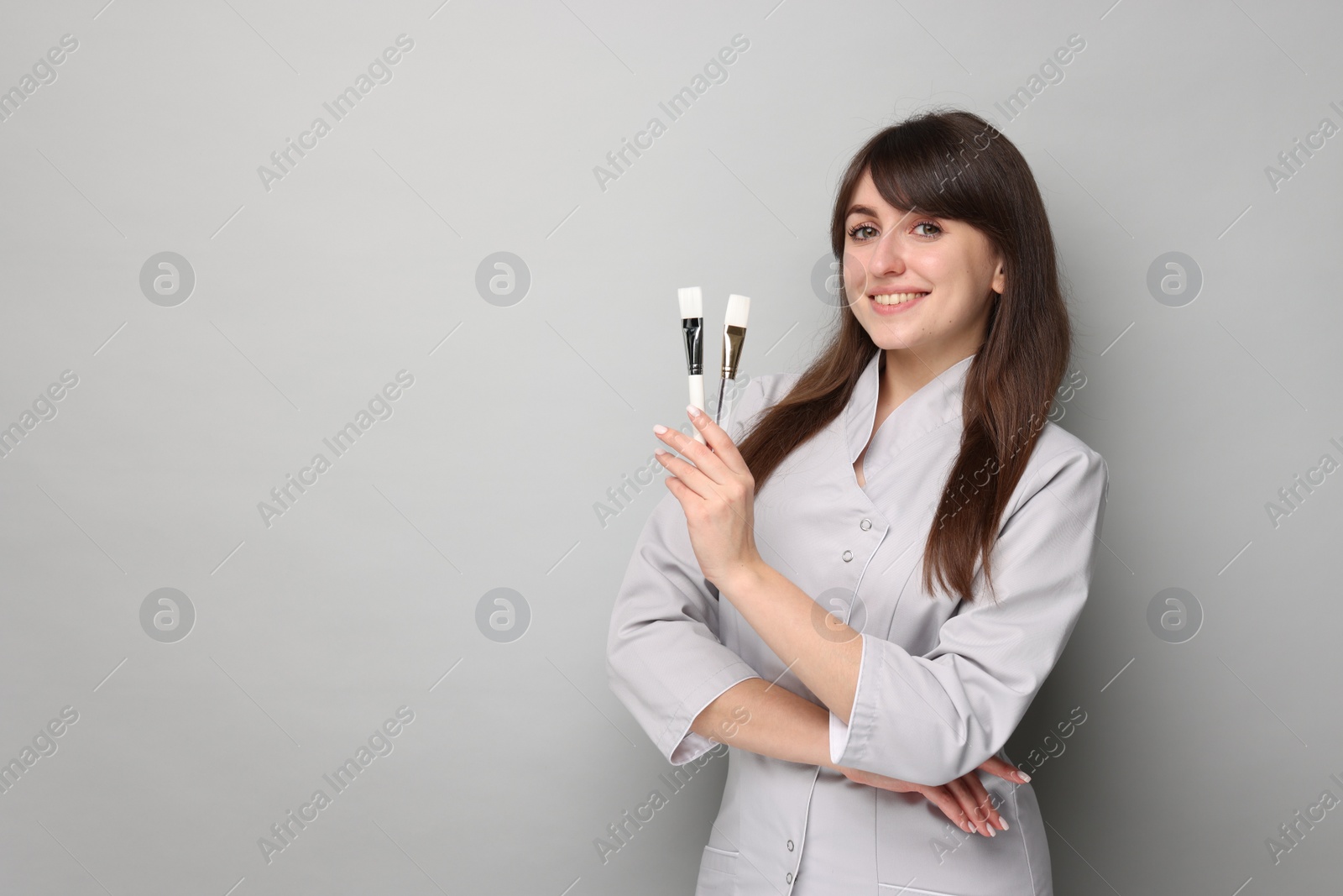 Photo of Cosmetologist with cosmetic brushes on grey background, space for text