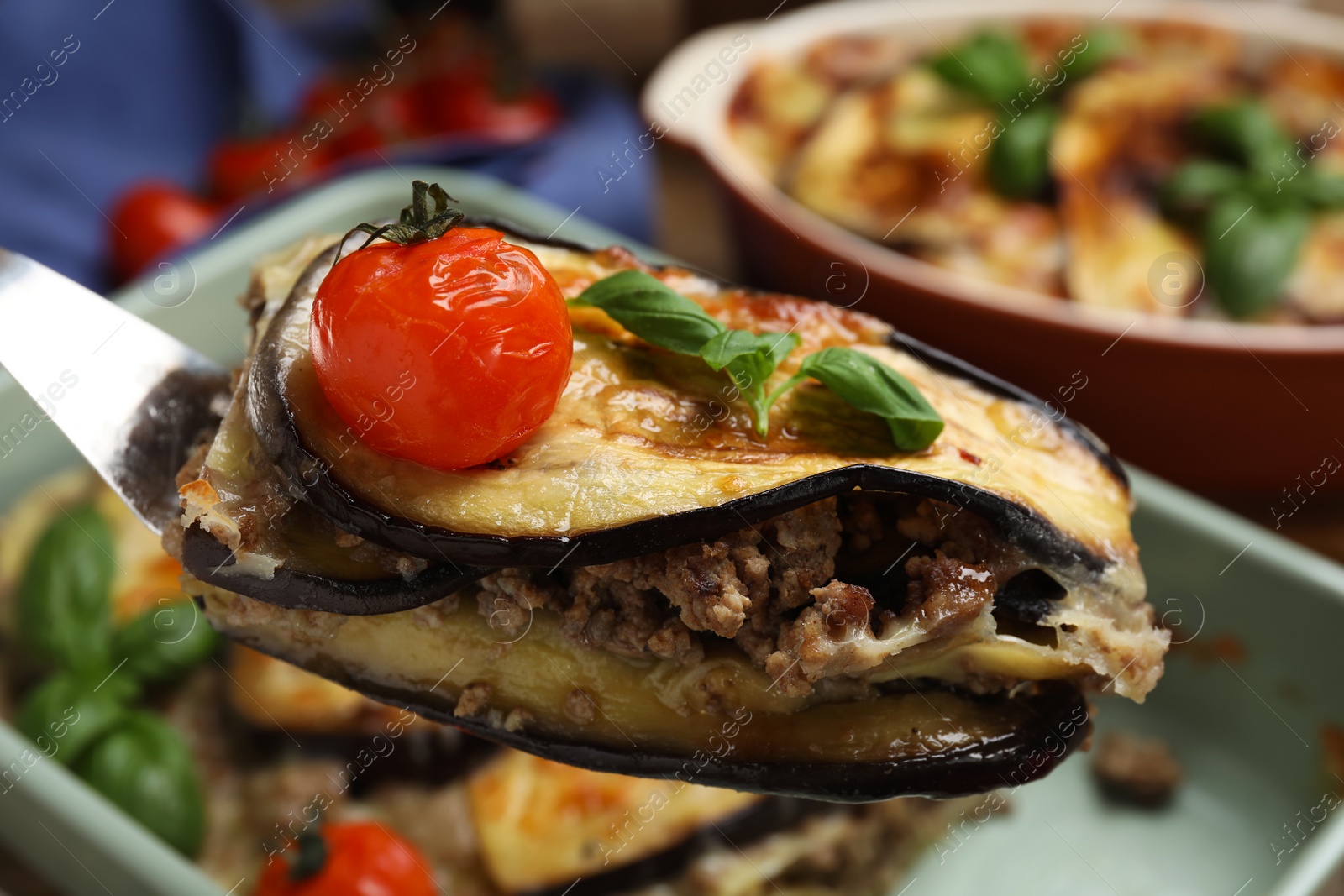 Photo of Spatula with piece of delicious eggplant lasagna over baking dish, closeup