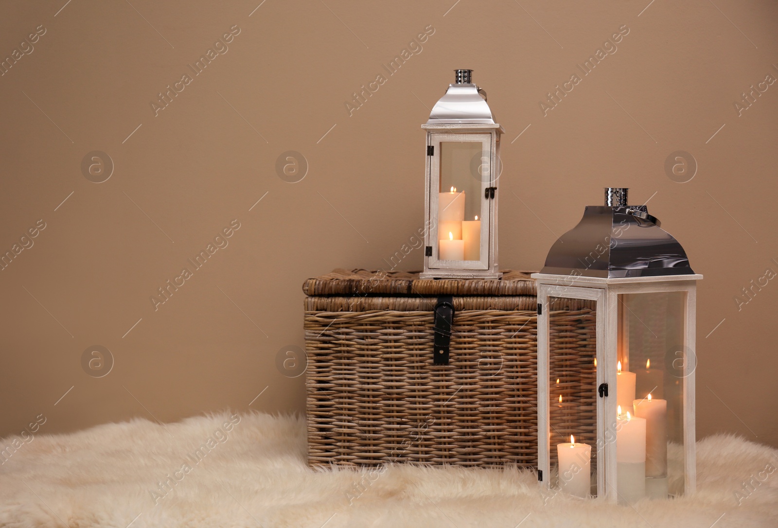 Photo of Decorative lanterns and wicker chest on fuzzy rug near brown wall, space for text. Interior elements
