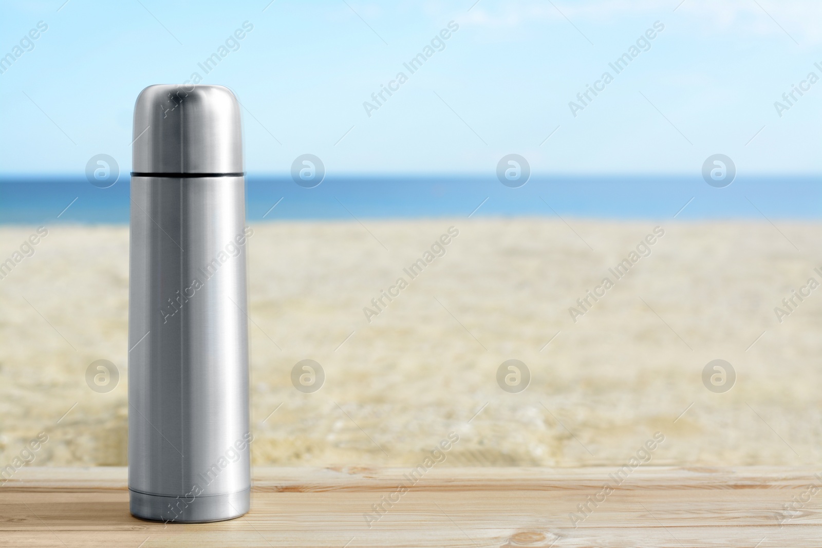 Photo of Metallic thermos with hot drink on wooden surface near sea, space for text