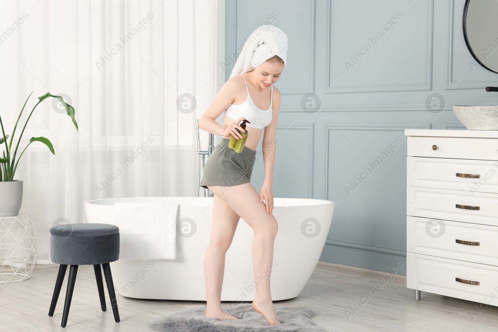 Photo of Beautiful young woman applying oil onto leg in bathroom