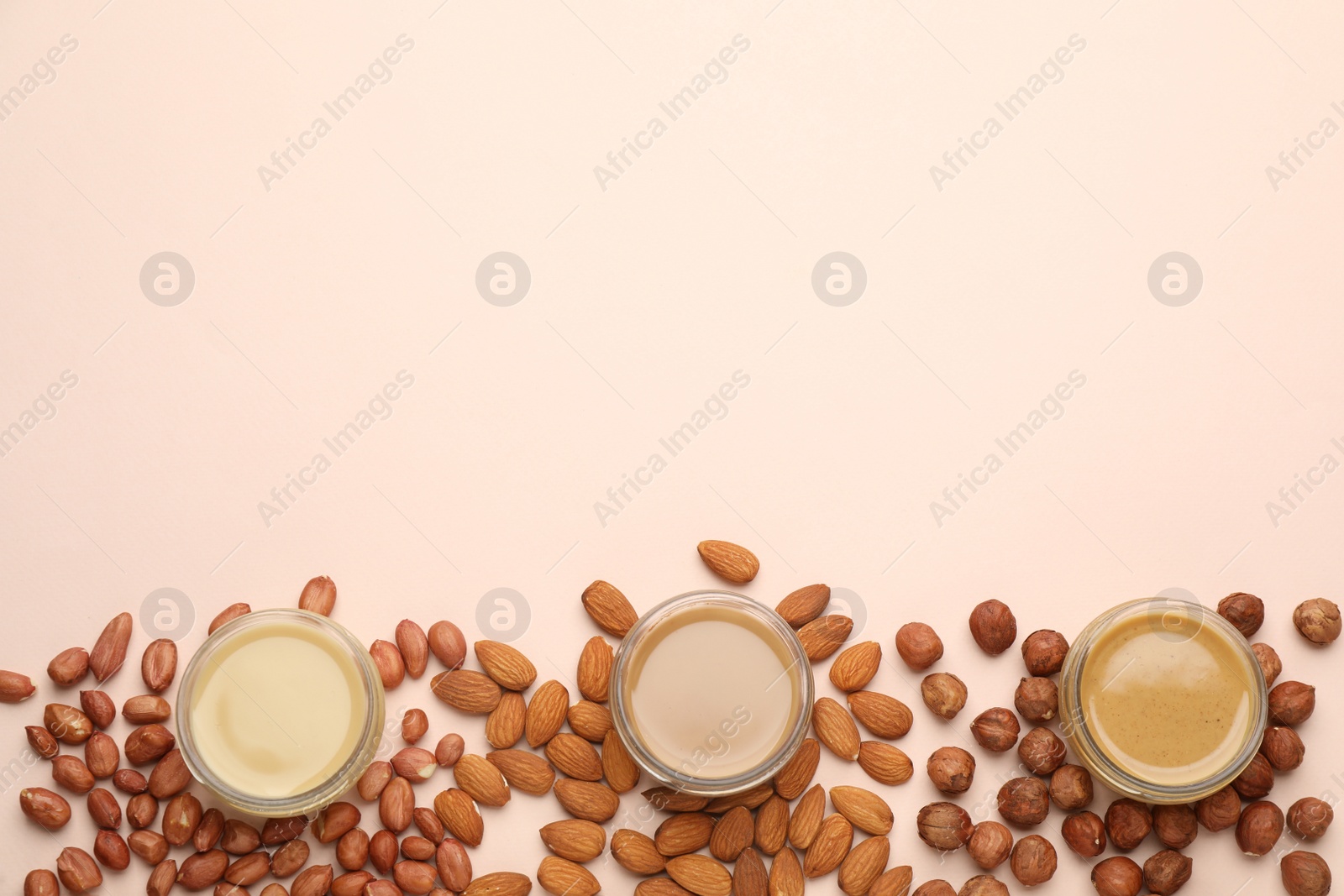 Photo of Different types of delicious nut butters and ingredients on beige background, flat lay. Space for text