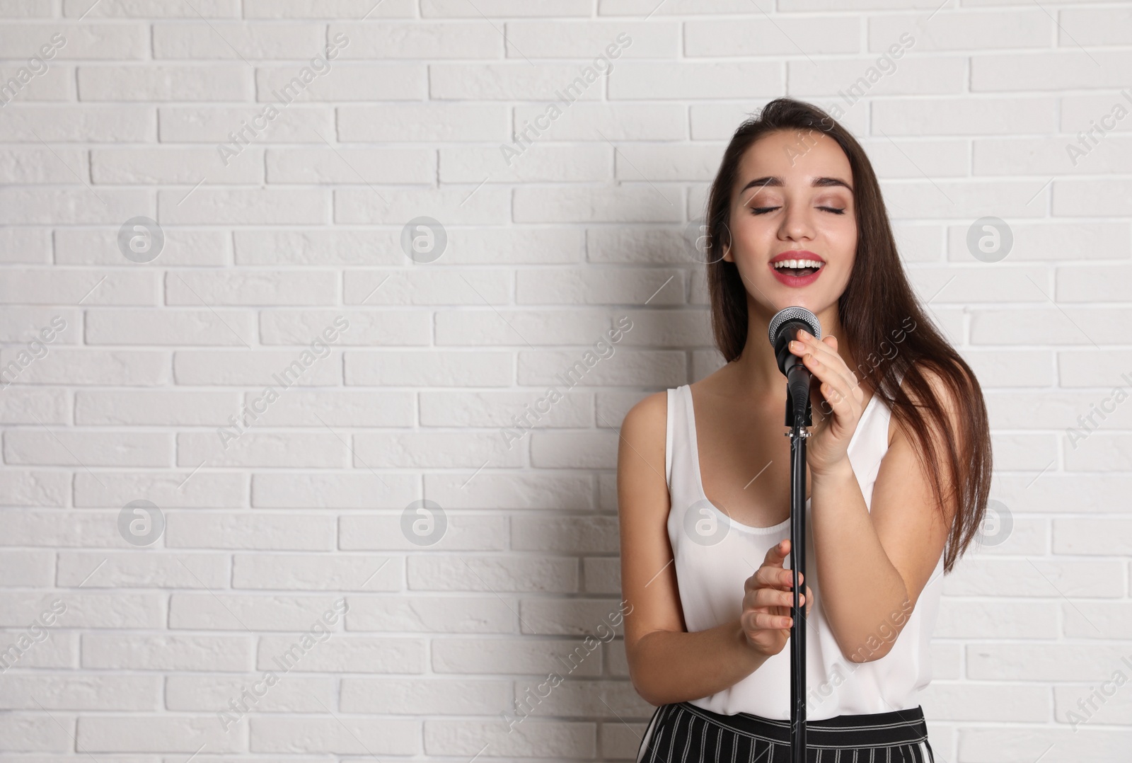 Photo of Young woman wearing casual clothes singing in microphone near brick wall. Space for text