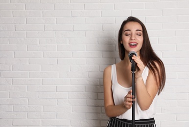 Young woman wearing casual clothes singing in microphone near brick wall. Space for text