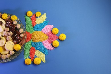 Diwali celebration. Tasty Indian sweets, colorful rangoli and chrysanthemum flowers on blue table, flat lay. Space for text