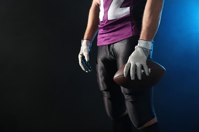 American football player with ball on dark background, closeup. Space for text